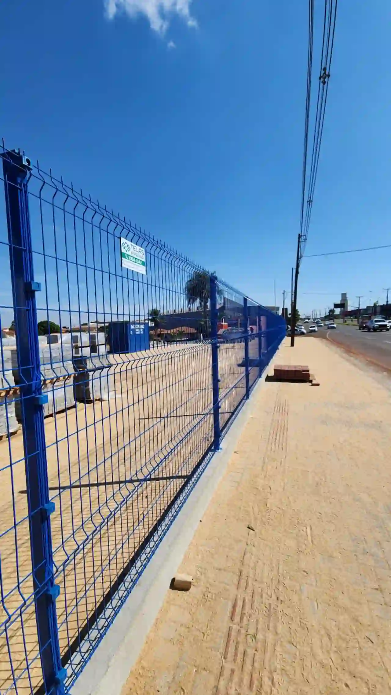 Gradil azul em terreno ao longo de avenida com palmeiras